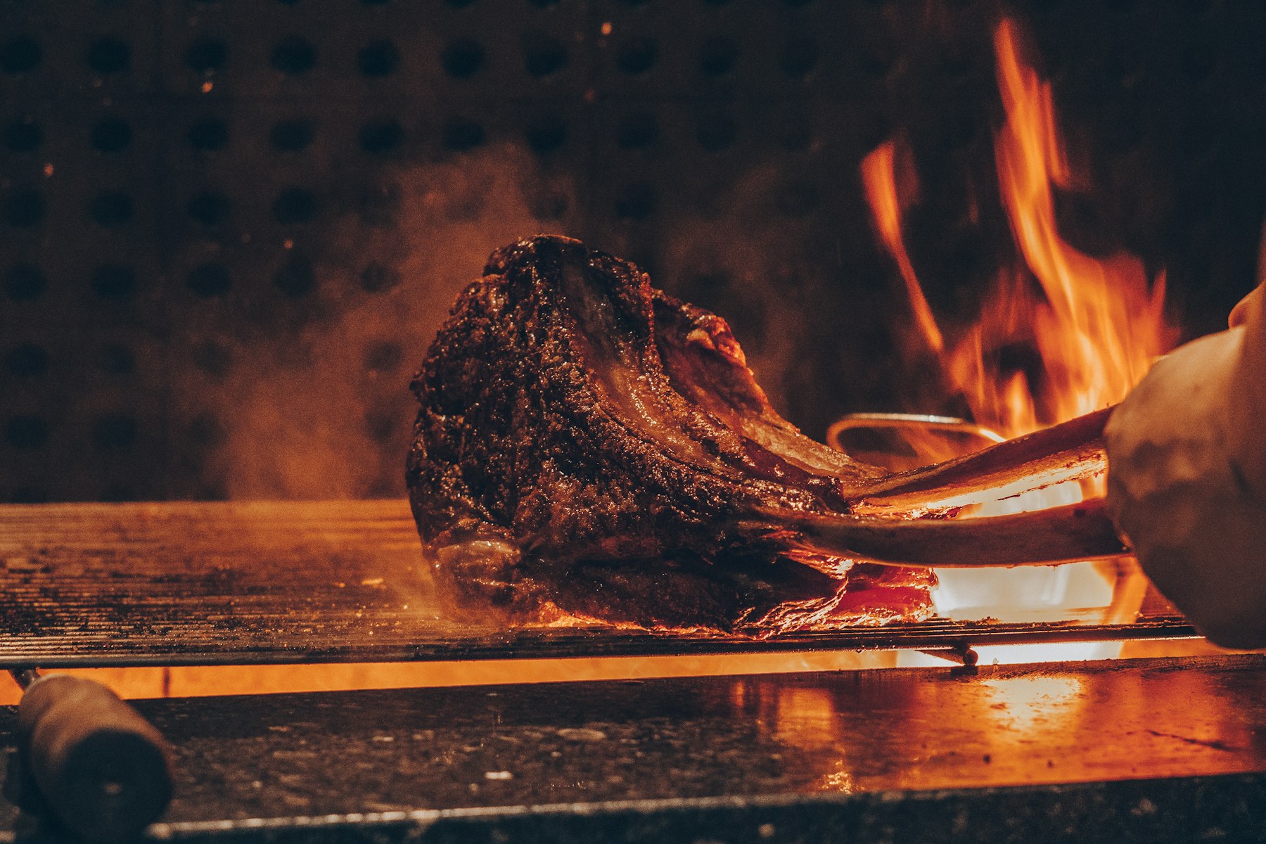 Long-bone tomahawk steak searing over an open grill flame